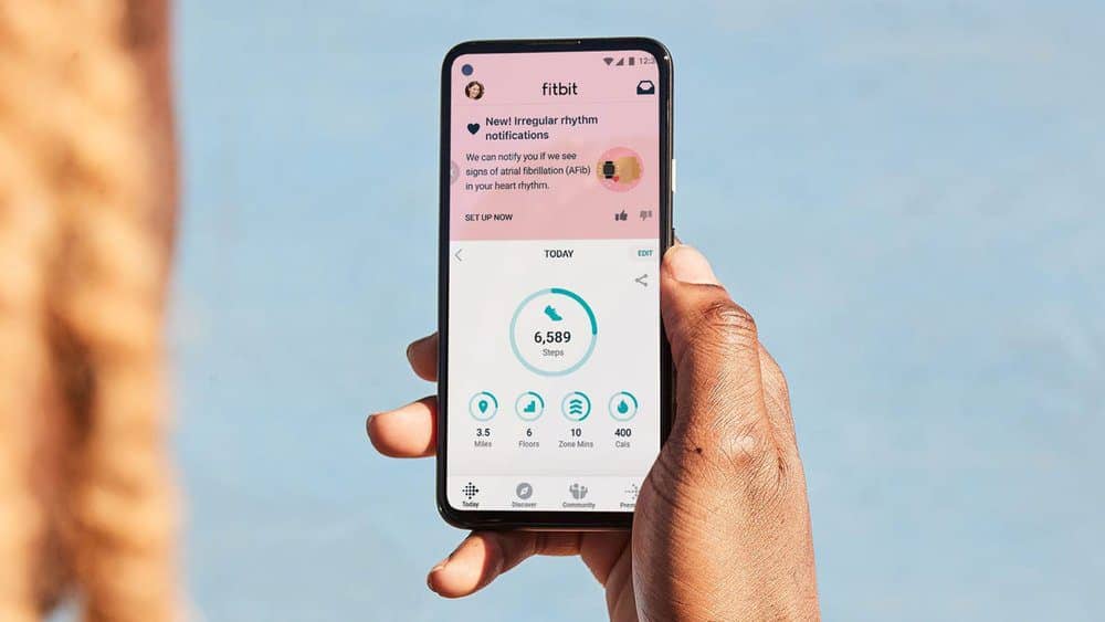 Fitbit app on phone held by a person in front of blue background