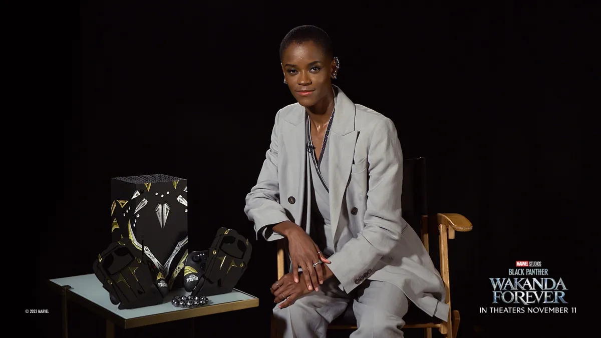 Letitia Wright posando ao lado do console Xbox Series X inspirado em Black Panther: Wakanda Forever, controles, suportes de controle e uma réplica de contas Kimoyo